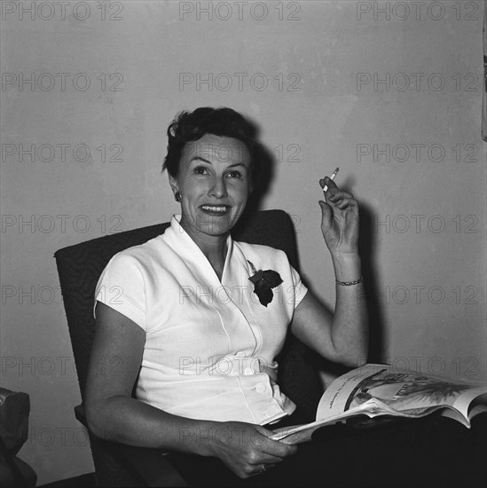 Mrs Douthwaite smoking. Mrs Douthwaite enjoying a cigarette whilst reading a magazine. Kenya, 21 September 1954. Kenya, Eastern Africa, Africa.