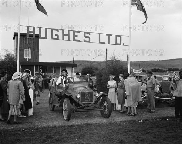 Hughes Ltd. Hughes Ltd at the Royal Show. A cheerful group surrounds a man in a vintage car. Nakuru, Kenya, 1 October 1954. Nakuru, Rift Valley, Kenya, Eastern Africa, Africa.