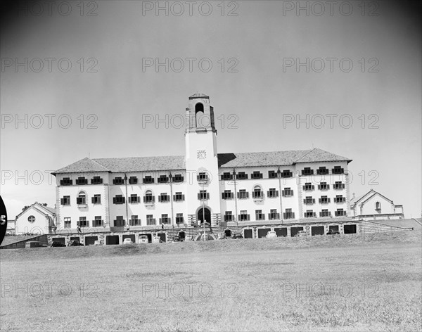 Clock tower at Makerere Hill. A large building with numerous windows and a prominent clock tower is surrounded by open grounds in the district of Makerere Hill. Kampala, Uganda, 12 October 1954. Kampala, Central (Uganda), Uganda, Eastern Africa, Africa.