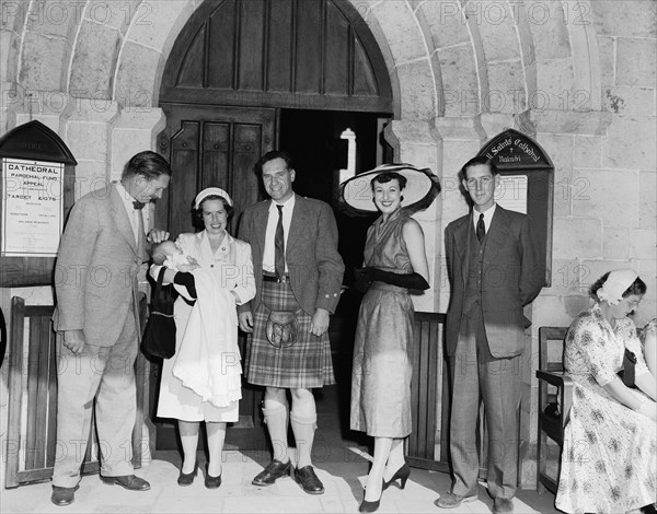 Nairobi christening. Family group gathered outside the entrance to All Saint's Church for the christening of Peter Buchanan's baby. Peter Buchanan is pictured wearing a tartan kilt and sporran. Nairobi, Kenya, 23 October 1954. Nairobi, Nairobi Area, Kenya, Eastern Africa, Africa.