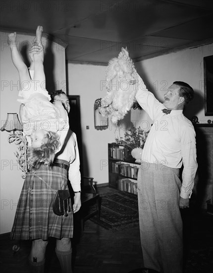Mine has four legs. High jinks on the christening of Peter Buchanan's baby. Interior shot of two men, one is holding a child upside down by the leg, the other holds a dog upside down by its tail. Nairobi, Kenya, 23 October 1954. Nairobi, Nairobi Area, Kenya, Eastern Africa, Africa.