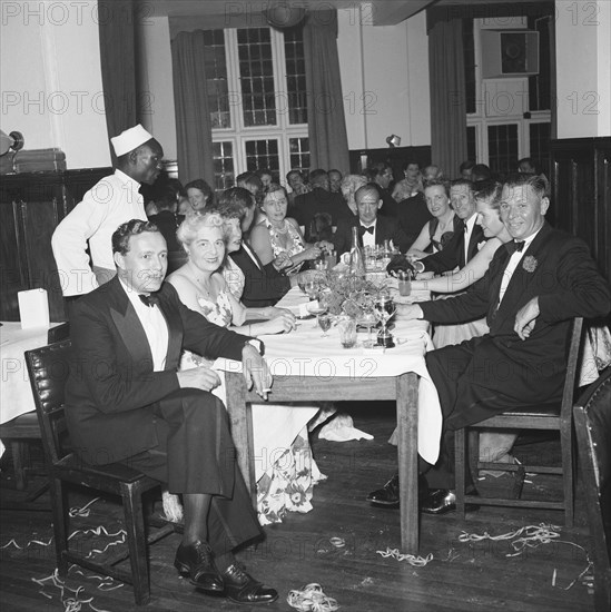 Motor sports dance. Formally dressed guests sit around tables enjoying drinks at a prize presentation evening. The tables are messy and party string litters the floor. Kenya, 26 November 1954. Kenya, Eastern Africa, Africa.