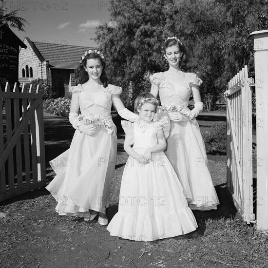 Three bridesmaids. Three bridesmaids at the Schofield-Sturman wedding pictured outside the entrance to a churchyard in Kabete, outside Nairobi. 
Kabete, Kenya, 11 December 1954., Nairobi Area, Kenya, Eastern Africa, Africa.