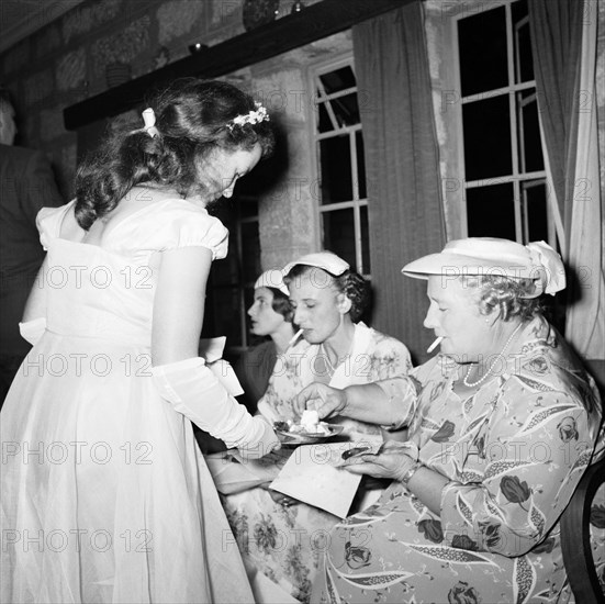 Anyone for cake?. A bridesmaid offers cake to a group of smoking female guests at the Schofield-Sturman wedding. Kambete, Kenya, 11 December 1954., Central (Kenya), Kenya, Eastern Africa, Africa.