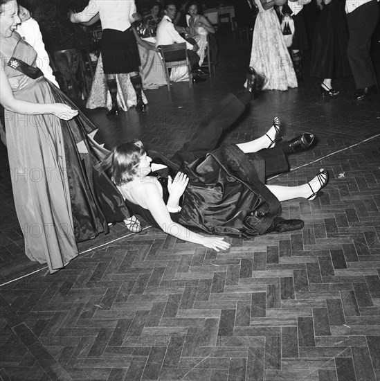 Trip, stumble and fall. A couple captured falling over on the dancefloor at the GHQ dance. The guests surrounding them are laughing. Kenya, 17 December 1954. Kenya, Eastern Africa, Africa.