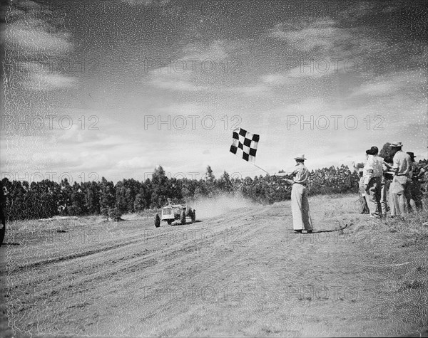 Waving the chequered flag. A man waves a chequered flag as a Lancia racing car crosses the finishing line in race number eight at the Eldoret race meeting. Eldoret, Kenya, 27 December 1954. Eldoret, Rift Valley, Kenya, Eastern Africa, Africa.
