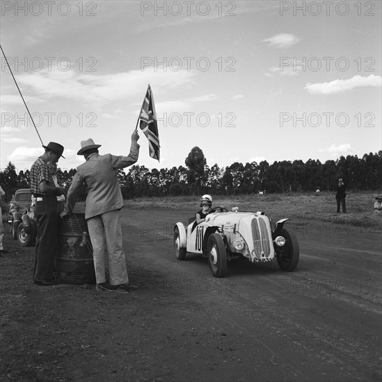 On your marks. A man holds up a union jack flag for car number 101, an Anglia Special, at the start of race eleven at the Eldoret race meeting. Eldoret, Kenya, 27 December 1954. Eldoret, Rift Valley, Kenya, Eastern Africa, Africa.