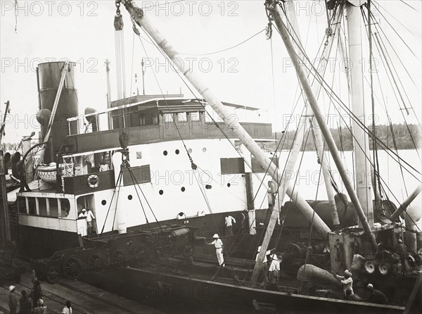 Unloading a bogie from SS Harmonides. Close up view of the cranes onboard SS Harmonides lowering a power bogie onto the dockside at Kilindini harbour. Mombasa, Kenya, circa 1926. Mombasa, Coast, Kenya, Eastern Africa, Africa.
