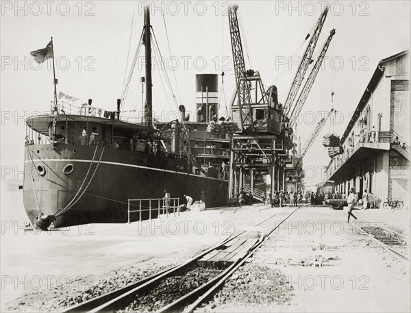 Loading grain on SS Modasa. SS Modasa docked at Kilindini harbour. Mombasa, Kenya, circa 1930. Mombasa, Coast, Kenya, Eastern Africa, Africa.