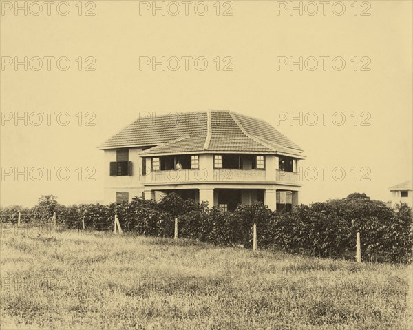 Railway house and garden. A railway house, property of the Kenya & Uganda Railways, used to accommodate senior British employees. At the time of the photograph it was home to Parlane Macfarlane (the man on the balcony), an engineer with KUR. Mombasa, Kenya, circa 1930. Mombasa, Coast, Kenya, Eastern Africa, Africa.