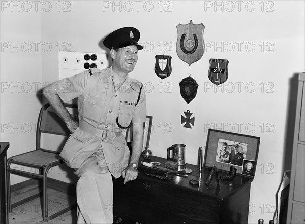 Jasper Maskelyne and his trophies. Jasper Maskelyne as a Kenyan Police officer proudly poses next to a selection of trophies and memorabilia. The shoulder epaulettes on his uniform read 'KENYA POLICE' and his shirt displays numerous military medals. Kenya, 24 February 1953. Kenya, Eastern Africa, Africa.