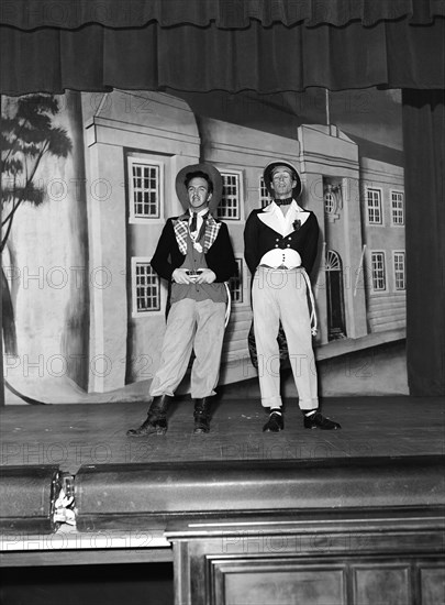 What a bore'. Wearing theatrical costume, Fred and Watson perform their 'What a bore' act on stage against a painted backdrop. One of several acts performed in a show called 'Re-face it'. Kenya, 24 February 1953. Kenya, Eastern Africa, Africa.