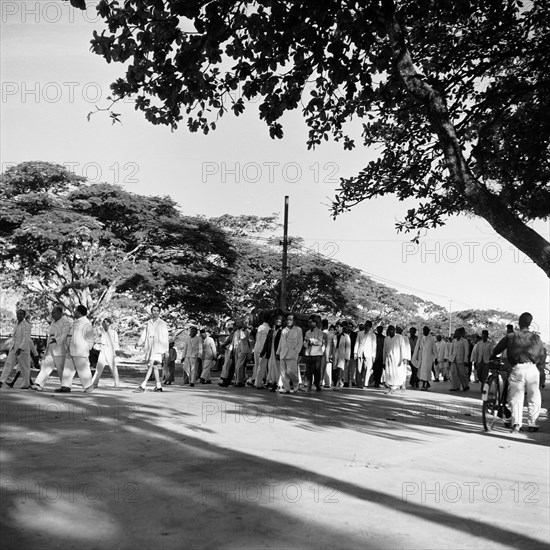 Zanzibar funeral. An all male funeral procession dressed predominantly in white, makes its way along a main street with a coffin covered by a dark cloth. Zanzibar (Tanzania), 3-12 March 1953., Zanzibar Central/South, Tanzania, Eastern Africa, Africa.