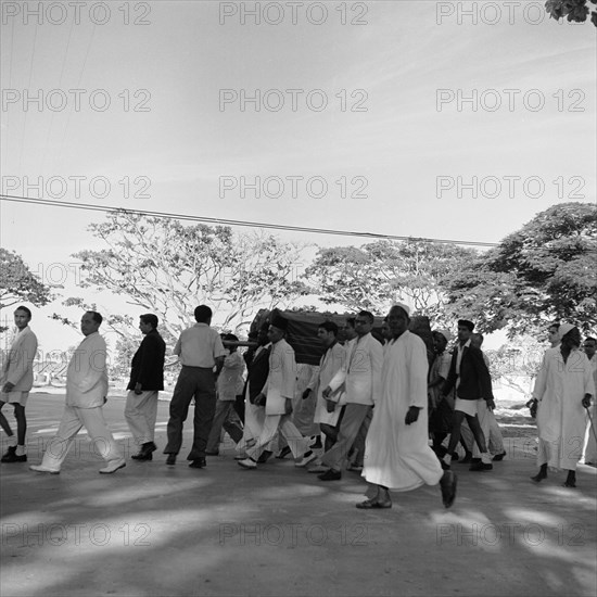 Zanzibar funeral. An all male funeral procession dressed predominantly in white, makes its way along a main street with a coffin covered by a dark cloth. Zanzibar (Tanzania), 3-12 March 1953., Zanzibar Central/South, Tanzania, Eastern Africa, Africa.