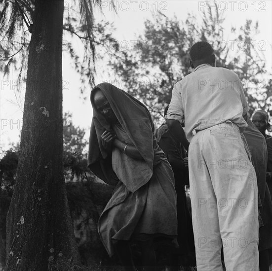 Woman at a cleansing ceremony. A woman at a cleansing ceremony, wrapped in cloth with her head covered. Kenya, 20-28 March 1953. Kenya, Eastern Africa, Africa.