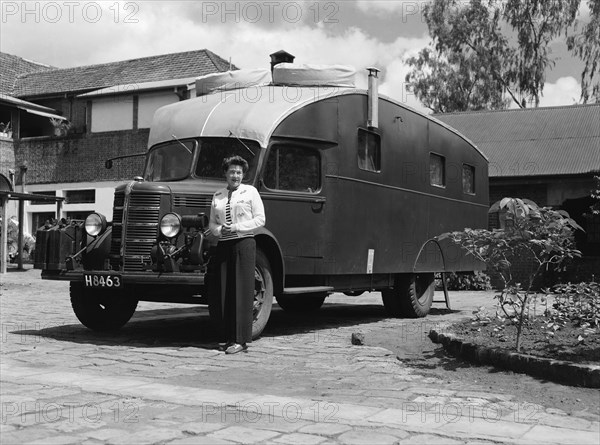 The Price's caravan. A woman stands with her hands clasped beside an old-fashioned caravan in the driveway to large house. Kenya, 12 May 1953. Kenya, Eastern Africa, Africa.