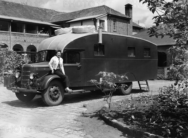 The Price's caravan. A woman sits on the wheel-arch of an old-fashioned caravan in the driveway to large house. Kenya, 12 May 1953. Kenya, Eastern Africa, Africa.