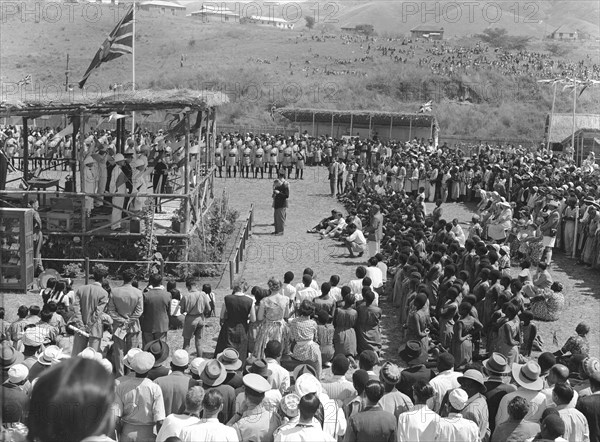 Mbeya show opening speech. A large, mixed race crowd watch the opening speech at the Mbeya show. A union jack flag flies above the speaker's podium. Mbeya, Tanganyika Territory (Tanzania), 28 August 1953. Mbeya, Mbeya, Tanzania, Eastern Africa, Africa.