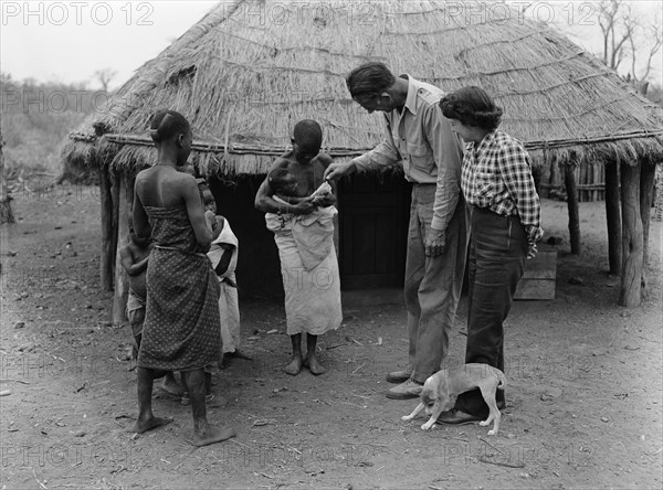 The Prices in Mozambique. An African family introduce their baby to a European couple, the Prices, beside a thatched hut. Mozambique, September 1953. Mozambique, Southern Africa, Africa.