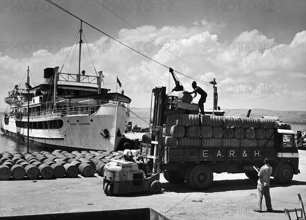 Unloading cotton bales at Lake Albert. A publicity photograph from the East African Railways and Harbours Administration (EAR&H) showing workers unloading bales of cotton from an EAR&H freight truck onto a wharf at Lake Albert. Western Division, Uganda, circa 1955., West (Uganda), Uganda, Eastern Africa, Africa.