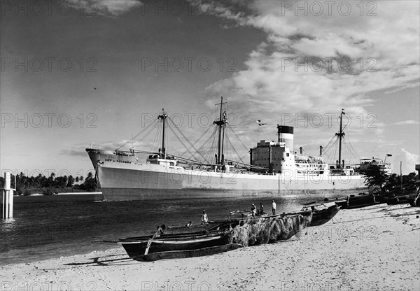 Old versus new. A publicity photograph from the East African Railways and Harbours Administration (EAR&H) showing the contrast between traditional fishing boats on the beach and the huge cargo ship 'City of Colombo' moored behind them. Dar es Salaam, Tanganyika Territory (Tanzania), circa 1960. Dar es Salaam, Dar es Salaam, Tanzania, Eastern Africa, Africa.