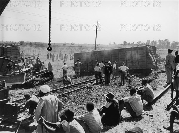 Aftermath of a train crash. An official photograph from the East African Railways and Harbours Administration (EAR&H) showing railway officials and workers surveying the aftermath of a train crash. A freight carriage is sprawled across the railway line: cranes and bulldozers have been brought in to clear the line. Probably Kenya, circa 1950. Kenya, Eastern Africa, Africa.