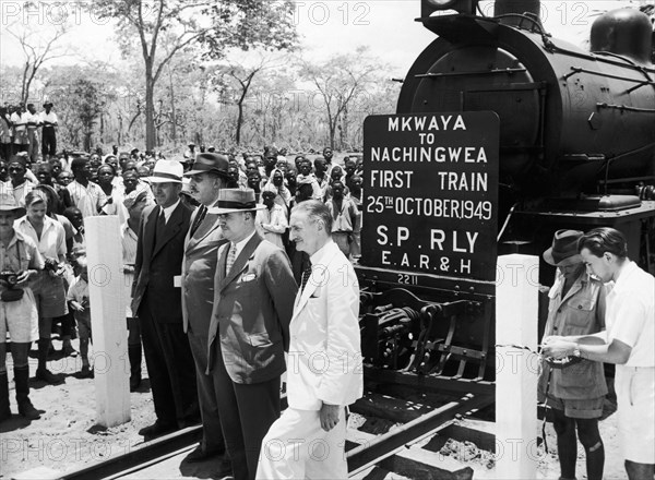 First train to Nachingwea. A publicity photograph from the East African Railways and Harbours Administration (EAR&H) shows four European railway officials posing on the track in front of a steam locomotive, which bears a plate announcing that it is the first train from Mkwaya to Nachingwea. Tanganyika Territory (Tanzania), 25 October 1949. Tanzania, Eastern Africa, Africa.