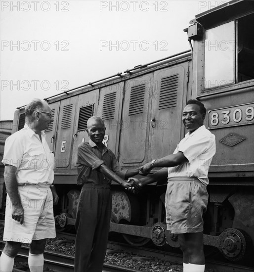 Railway workers shake hands. A publicity photograph from the East African Railways and Harbours Administration (EAR&H) showing two of its African employees shaking hands and smiling for the camera in front of a train, locomotive number 8309. Mombasa, Kenya, circa 1960. Mombasa, Coast, Kenya, Eastern Africa, Africa.