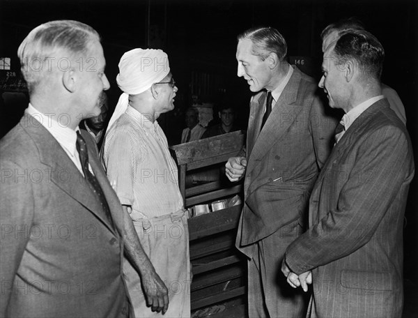 Sir Evelyn Baring talks to a railway worker. A publicity photograph from the East African Railways and Harbours Administration (EAH&R) showing Sir Evelyn Baring (middle right), Governor of Kenya, chatting with an elderly Indian man. European railway officials are also present. Kenya, circa 1955. Kenya, Eastern Africa, Africa.