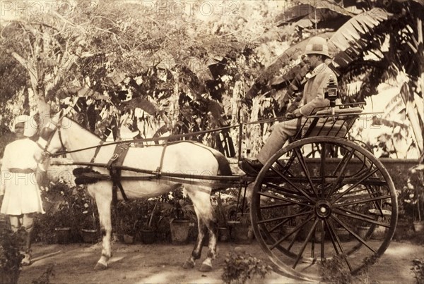 Two-wheeled carriage. A British gentleman in a solaptopi hat sits aboard a two-wheeled carriage holding the reins of a grey horse. An Indian servant holds the horse's bridle. India, circa 1880. India, Southern Asia, Asia.