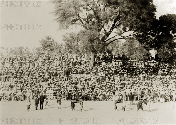 Indian wrestling competition. A large audience of turbaned Indian men gather on a slope to watch a wrestling match between local men. Three pairs of semi-naked combatants can be seen entertaining the crowd in an open arena. India, circa 1880. India, Southern Asia, Asia.