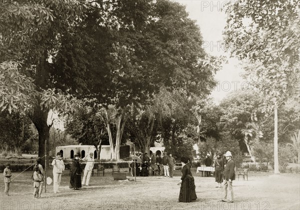 Mixed-sex tennis match. A small gathering of onlookers watches a tennis match between a group of British men and women. Turbaned Indian ball boys wait at the sides of the net, ready to catch any stray shots. India, circa 1880. India, Southern Asia, Asia.