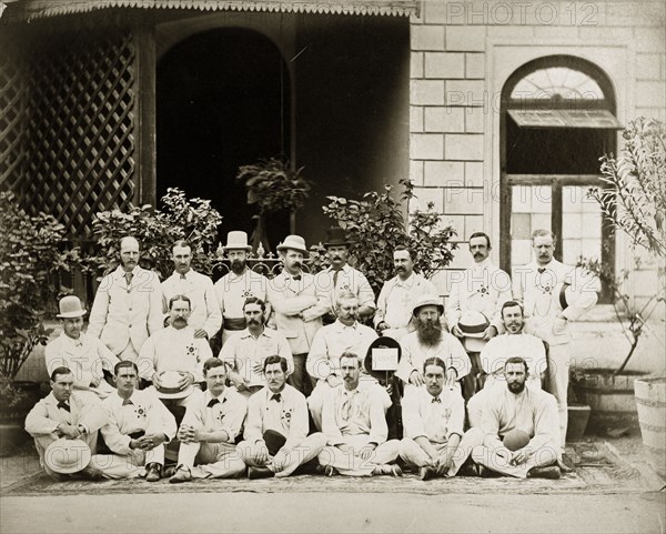 Bombay cricket teams. Group portrait of the north and south Bombay cricket teams dressed in their whites outside a colonial-style residency building. A man idenitifed as 'S. Fellowes' holds up a hat on a stick with a sign that reads 'Caldecott', the name of an absent team member. Bombay (Mumbai), India, circa 1875. Mumbai, Maharashtra, India, Southern Asia, Asia.