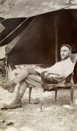 European camper. A European man relaxing in a chair outside his tent, looks up from the letter he is reading. Possibly Burma (Myanmar), South East Asia, 1908., South East Asia, Asia.