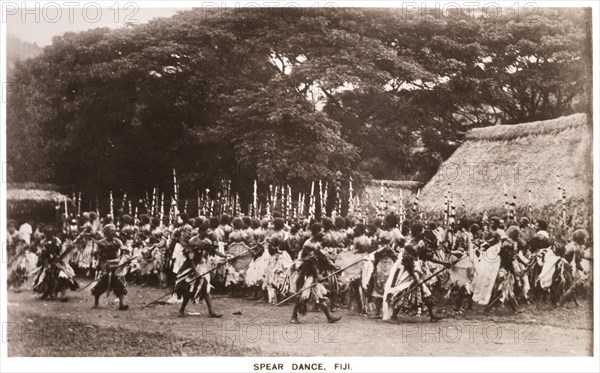 Performing a 'meke wesi'. A crowd of male Fijian dancers dressed in ceremonial costume perfom a traditional 'meke wesi' dance with spears. Fiji, circa 1920. Fiji, Pacific Ocean, Oceania.