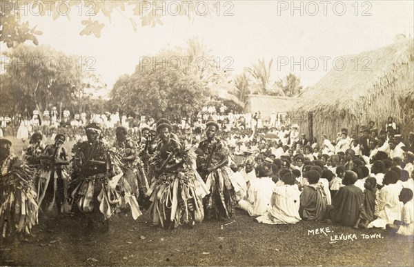 A traditional Fijian 'meke'. A crowd watches as a group of male Fijian dancers dressed in ceremonial costume perform a traditional 'meke'. Levuka, Fiji, circa 1920. Levuka, Ovalau, Fiji, Pacific Ocean, Oceania.