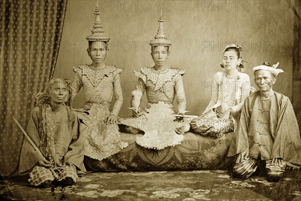 Burmese court performers. Studio portrait of a group of Burmese court performers and attendants, employees of the Royal Palace in Mandalay. The two crowned men and the kneeling woman are dressed in elaborate costumes as the characters from the popular Hindu epic, the 'Ramayana'. Probably Mandalay, Burma (Myanmar), circa 1878. Burma (Myanmar), South East Asia, Asia.