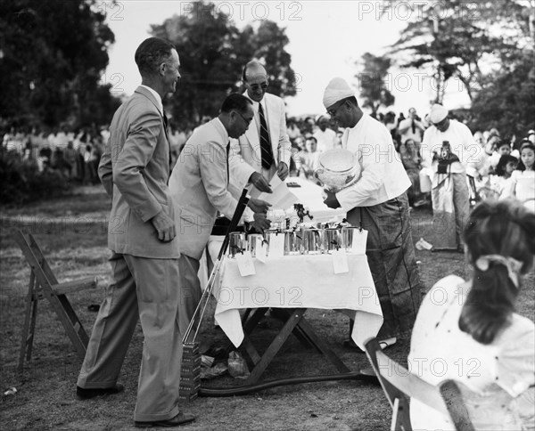 U Zin nearly dropping the Cup'. The President of the Rangoon Golf Club awards the Kyaw Min Cup (an award in the Burma Open Championship) to a club council member identified as 'U Zin'. According to the original caption, the jovial mood of the men is due to 'U Zin nearly dropping the Cup'. Rangoon (Yangon), Burma (Myanmar), circa 1952. Yangon, Yangon, Burma (Myanmar), South East Asia, Asia.