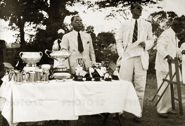 Burma Open Championship awards. R.B. Groves, a Captain of the Rangoon Golf Club, addresses an audience before handing over to the club's President at an awards ceremony for the Burma Open Championship. The pair stand behind a table laden with golf trophies. Rangoon (Yangon), Burma (Myanmar), circa 1952. Yangon, Yangon, Burma (Myanmar), South East Asia, Asia.
