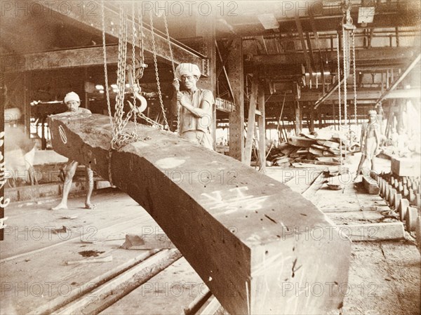 Manoevering teak logs at a timber yard. Two labourers manoeuvre a processed timber beam using a chain pulley system at a timber yard. Burma (Myanmar), circa 1910. Burma (Myanmar), South East Asia, Asia.