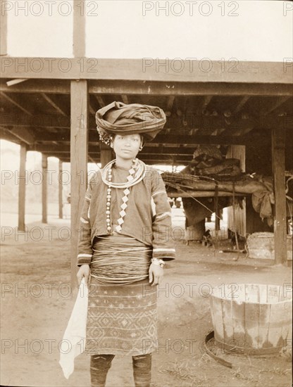 Kachin woman in traditional dress. Portrait of a Kachin woman dressed in traditional costume. She wears multiple hoops that encircle her waist and neck, and a cloth scarf wrapped around her head. Kachin State, Burma (Myanmar), circa 1910., Kachin, Burma (Myanmar), South East Asia, Asia.