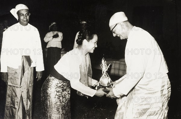 Receiving a 'Na-Ya' award. A European employer, dressed in a traditional Burmese 'longyi', is presented with a silver 'Na-Ya' award by Mrs Melvin Tun Pe. Burma (Myanmar), circa 1955. Burma (Myanmar), South East Asia, Asia.