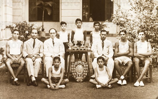 Sports team at the Royal College of Colombo. Outdoors portrait of a sports team with their trophies at the Royal College of Colombo. The players pose in their sports kit with three members of college staff, including Edward Lawrence Bradby, College Principal between 1939 and 1945. Colombo, Ceylon (Sri Lanka), circa 1942. Colombo, West (Sri Lanka), Sri Lanka, Southern Asia, Asia.