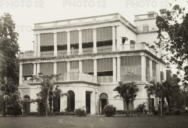 facade of a colonial-style building. The colonnaded facade of a two-storey, colonial building, featuring a projecting front porch, and a square tower at the rear. Probably India, circa 1950. India, Southern Asia, Asia.