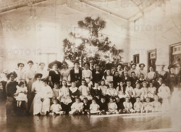 Hong Kong Christmas. Children belonging to European staff of the Taikoo Dockyard pose with their parents for a group portrait in front of a large Christmas tree. Hong Kong, China, December 1910. Hong Kong, Hong Kong, China, People's Republic of, Eastern Asia, Asia.