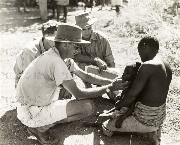 Doctor examining a child with sleeping sickness. A European medic, identified as Dr Cookson, is assisted by two others as he examines a young child suffering from sleeping sickness (African trypanosomiasis). Probably Northern Rhodesia (Zambia), circa 1950. Circa 1949. Zambia, Southern Africa, Africa.