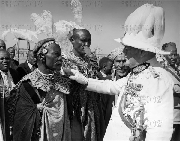 Sir Phillip Mitchell greets African chiefs. The Governor of Kenya, Sir Phillip Mitchell, greets African chiefs during Princess Elizabeth's visit to Kenya. Both wear traditional military regalia and ceremonial feathers on their heads. Mitchell displays numerous medals on his jacket: the chiefs wear animal skins and ornate jewellery. Kenya, February 1952. Kenya, Eastern Africa, Africa.