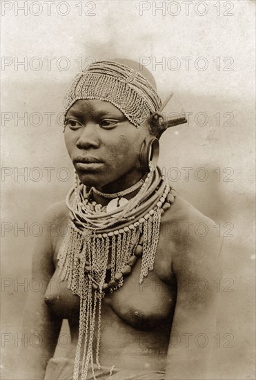 Kenyan woman in beaded headdress. Half-length portrait of a semi-naked woman wearing a beaded headdress, together with ornate neck and ear jewellery. The style of earrings suggests the woman may be Kikuyu. Kenya, circa 1930. Kenya, Eastern Africa, Africa.