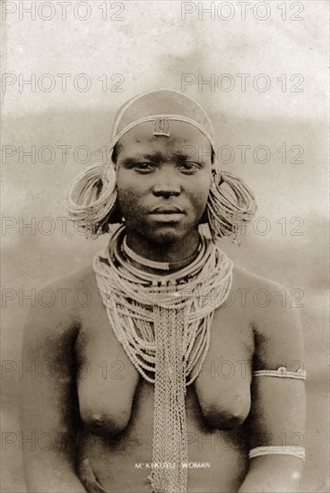 Kikuyu woman. Half-length portrait of a semi-naked Kikuyu woman wearing neck chains and heavy bunches of looped earrings. Kenya, circa 1930. Kenya, Eastern Africa, Africa.