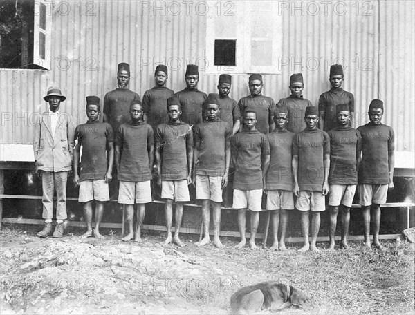 Employees of the Public Works Department. Group portrait of 17 African employees at the Public Works Department. All but one of the line-up wears a uniform consisting of shorts and a military-style jumper or sweater displaying the initials 'PWD' on the chest. British East Africa (Kenya), 1912., Nairobi Area, Kenya, Eastern Africa, Africa.